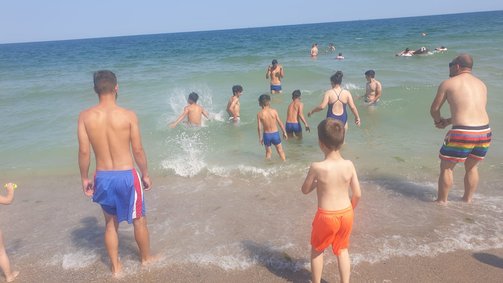 Copiii intrând în mare în tabăra de vară, văzuți din spate